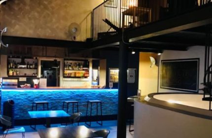Metro Sauna Centrale Milan bar area. Blue lit bar with stools, tables, and a mezzanine level. Gay sauna travel advice.
