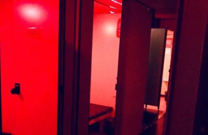 Interior of Metro Sauna Centrale Milan, a gay sauna. Red lighting illuminates private cabins with benches. Gay travel advice.