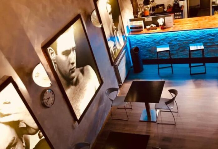 Metro Sauna Centrale Milan interior. Gay sauna's lounge area with bar, tables, chairs, and black & white photos of men on the walls.