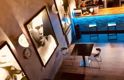 Metro Sauna Centrale Milan interior. Gay sauna's lounge area with bar, tables, chairs, and black & white photos of men on the walls.