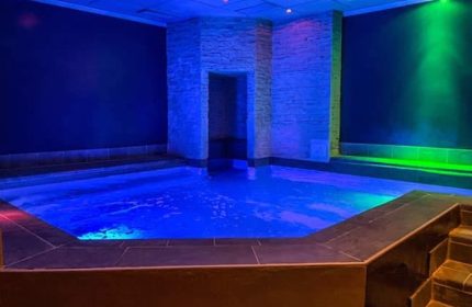 Metro Sauna Centrale Milan: Indoor pool with blue lighting, stone accents, and steps. Gay sauna for relaxation and socializing.