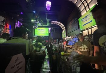 Midnight Sun Video Bar interior in San Francisco. Bartender, karaoke screen, and patrons. A lively gay bar for travelers.
