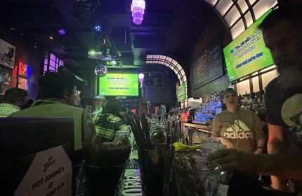 Midnight Sun Video Bar interior in San Francisco. Bartender, karaoke screen, and patrons. A lively gay bar for travelers.