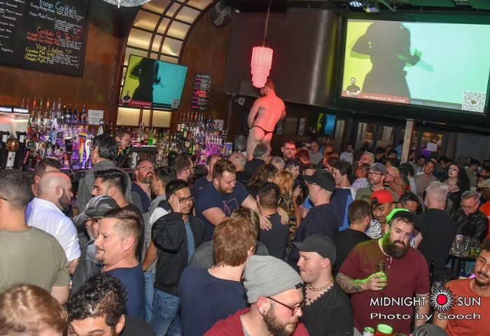 Midnight Sun Video Bar in San Francisco: A packed gay bar with men, drinks, and a dancer on a platform. A popular gay travel destination.