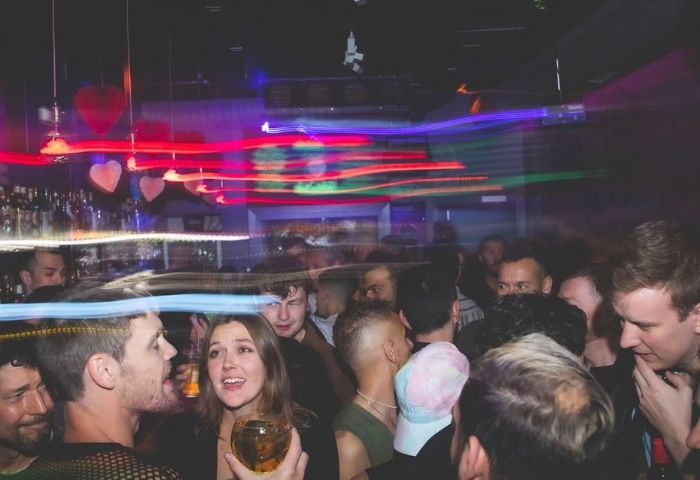 Crowded Moeem gay bar in Barcelona. People socializing and drinking under colorful lights. Popular spot for gay men's travel in Barcelona.