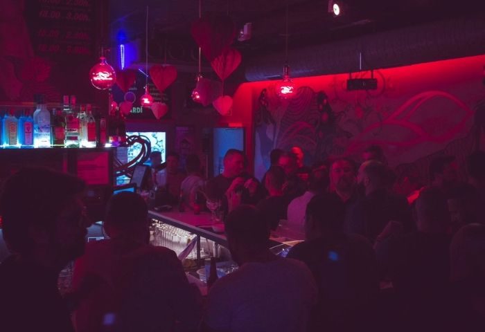 Moeem Gay Bar in Barcelona: Interior view of the bar with patrons, red lighting, and heart decorations. Gay nightlife travel advice.