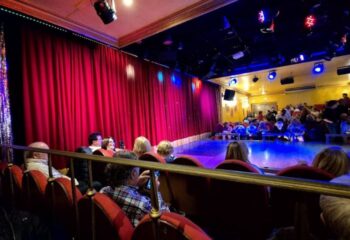 Molino Benidorm theater interior. Red curtains, stage lights, and audience seating. Gay live shows in Benidorm for gay men travel.