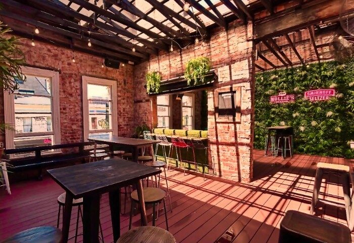 Mollie's Bar and Diner, Melbourne. Outdoor seating area with brick walls, wooden tables, and a green wall featuring neon signs. Gay travel.