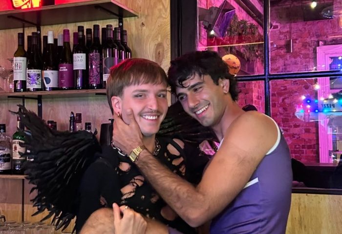 Two gay men smile at Mollie's Bar and Diner in Melbourne. One wears angel wings. Gay travel advice for Melbourne, Australia.