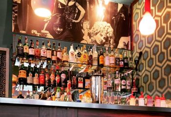 Mono Bar Milan: A stylish bar with shelves full of liquor bottles, vintage decor, and a retro vibe. A gay-friendly destination.