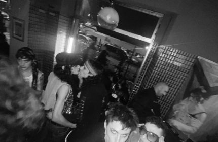Milan gay bar scene: Black and white shot of a crowded Mono Bar, with two men kissing and others enjoying the nightlife.