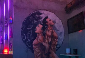 Shanghai gay bar: Moon Bar interior with a mural of two shirtless men in front of a moon. Bottles on a shelf with neon lights.