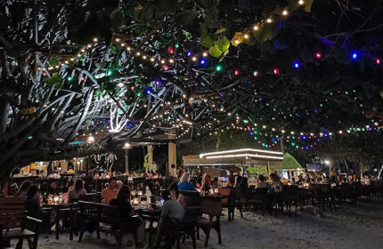 Beachfront dining at Tubtim Resort, a popular gay hotel near gay bars. Tables under trees are lit with colorful lights at night.