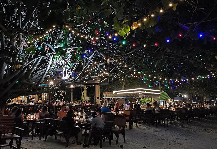 Beachfront dining at Tubtim Resort, a popular gay hotel near gay bars. Tables under trees are lit with colorful lights at night.