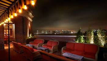 The Jane Hotel's rooftop bar at night, a most-booked budget gay hotel in New York City. Sofas, tables, lights, & a skyline view.