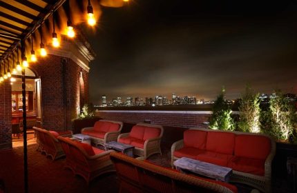 The Jane Hotel's rooftop bar at night, a most-booked budget gay hotel in New York City. Sofas, tables, lights, & a skyline view.