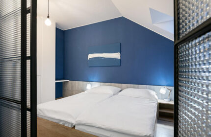 Meetme23 gay-friendly hostel: Private double beds room with blue wall, modern art, and textured glass partition. Comfortable gay travel lodging.