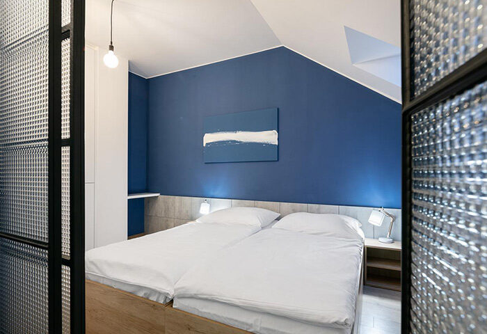 Meetme23 gay-friendly hostel: Private double beds room with blue wall, modern art, and textured glass partition. Comfortable gay travel lodging.