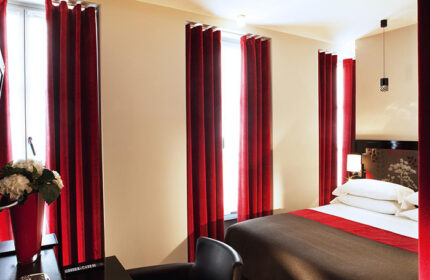 Hotel Caron, Paris room. Gay-friendly hotel with red curtains, bed, and desk. Most-booked for gay travelers in Paris. Interior design.