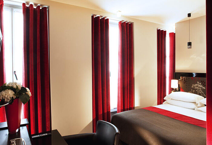Hotel Caron, Paris room. Gay-friendly hotel with red curtains, bed, and desk. Most-booked for gay travelers in Paris. Interior design.