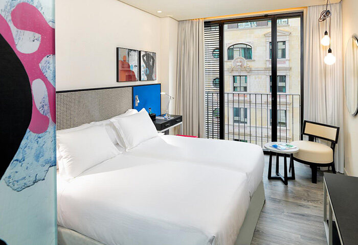 H10 Art Gallery Hotel, a most-booked gay-friendly hotel in Eixample, Barcelona. Room with twin beds, balcony, and city view. Modern art decor.