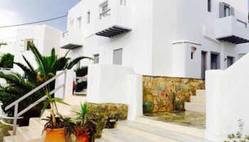 M for Mykonos gay-friendly hotel in Mykonos Town. White building with stairs, stone accents, and potted plants. Gay travel in Mykonos.