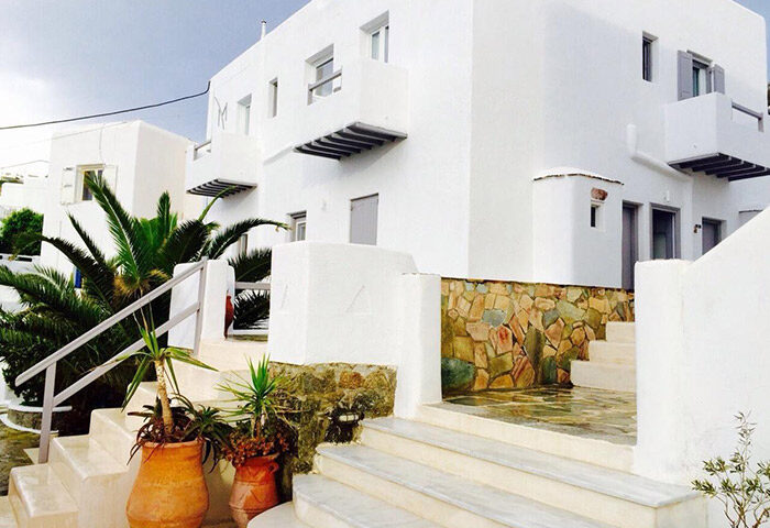 M for Mykonos gay-friendly hotel in Mykonos Town. White building with stairs, stone accents, and potted plants. Gay travel in Mykonos.