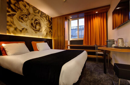 Hotel Elixir, a most-booked gay honeymoon hotel in Paris near gay nightlife. Room interior with bed, floral wall art, window, and desk.