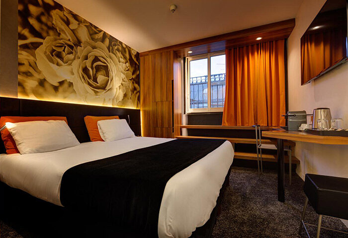 Hotel Elixir, a most-booked gay honeymoon hotel in Paris near gay nightlife. Room interior with bed, floral wall art, window, and desk.