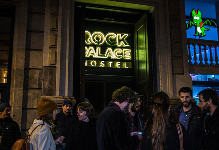 Sant Jordi Hostels Rock Palace, a popular gay hostel in Barcelona's Eixample near gay nightlife. Hostel entrance at night with a group of people.