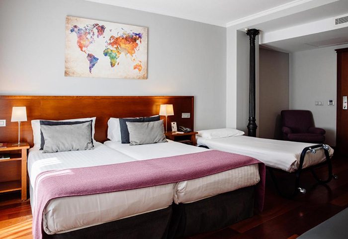 Hotel Infantas by MIJ room for 3 adults. Most booked gay hotel Madrid, features twin beds, a rollaway, and a colorful world map art piece.