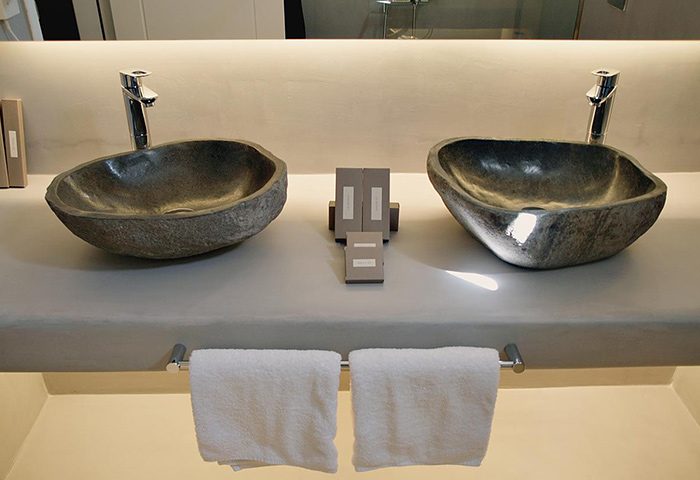 Ilio Maris gay hotel Mykonos: Stone sinks, towels, and toiletries in a modern bathroom. Near gay bars in Mykonos Town.