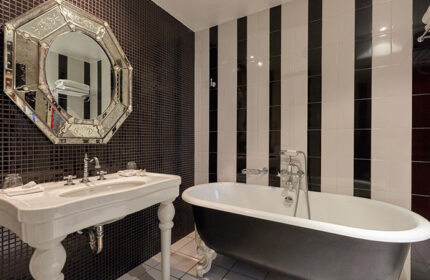 Hotel du Petit Moulin bathroom. Black & white striped tiles, black mosaic wall, vintage mirror, & clawfoot tub. Most-booked gay hotel in Paris.