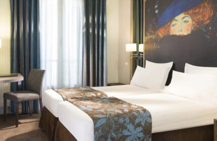Hotel Turenne Le Marais room, a most-booked gay hotel in Paris near gay nightlife. Twin beds with floral runner, Klimt portrait, desk and chair.