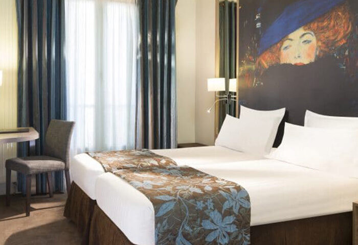 Hotel Turenne Le Marais room, a most-booked gay hotel in Paris near gay nightlife. Twin beds with floral runner, Klimt portrait, desk and chair.