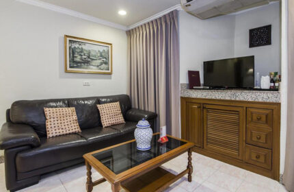Copa Hotel Pattaya living room. Most booked gay hotel. Leather couch with pillows, glass coffee table, TV, and wooden cabinet. Gay travel advice.