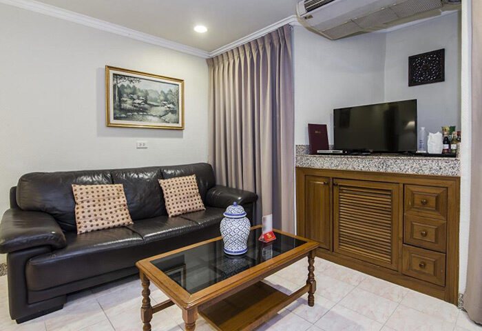 Copa Hotel Pattaya living room. Most booked gay hotel. Leather couch with pillows, glass coffee table, TV, and wooden cabinet. Gay travel advice.