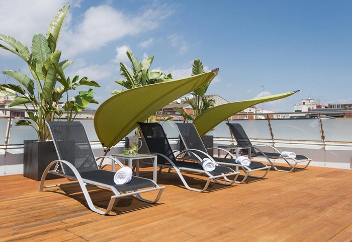 Ako Suites Hotel rooftop terrace with lounge chairs and sunshades. Most-booked gay hotel serviced apartment in Barcelona's gayborhood.