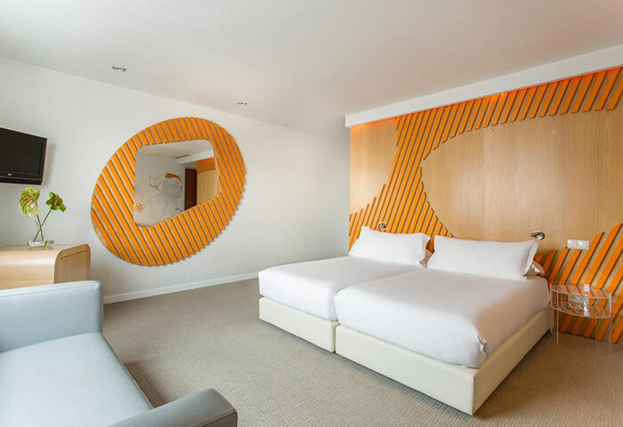 Room Mate Oscar hotel bedroom in Madrid's Chueca gayborhood. Modern design with twin beds, orange accents, and unique mirror. Top gay hotel.