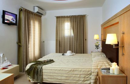 Matogianni Hotel room, Mykonos Town. Most booked gay hotel near gay bars. Queen bed, TV, hat, candles, and soft lighting. Relaxing vibe.