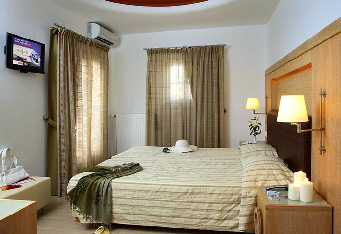 Matogianni Hotel room, Mykonos Town. Most booked gay hotel near gay bars. Queen bed, TV, hat, candles, and soft lighting. Relaxing vibe.