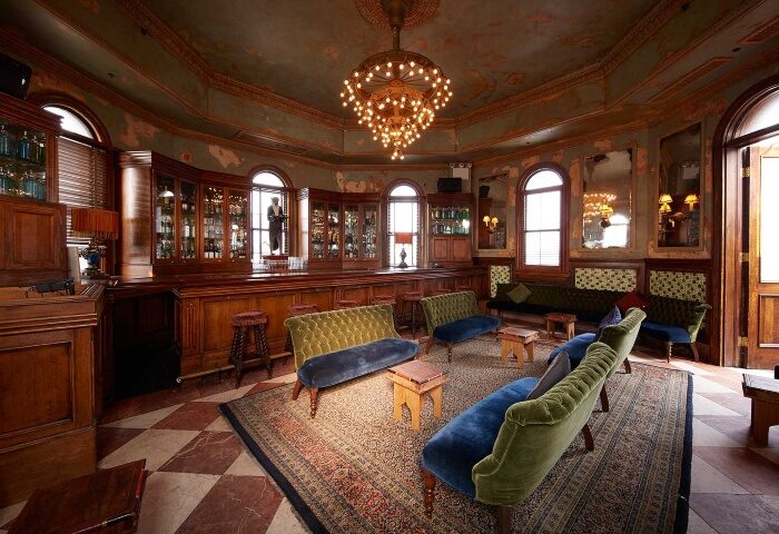 The Jane Hotel, a most-booked gay hotel near gay bars in New York City. Ornate bar area with velvet couches, chandelier, and vintage decor.