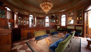 The Jane Hotel, a most-booked gay hotel near gay bars in New York City. Ornate bar area with velvet couches, chandelier, and vintage decor.