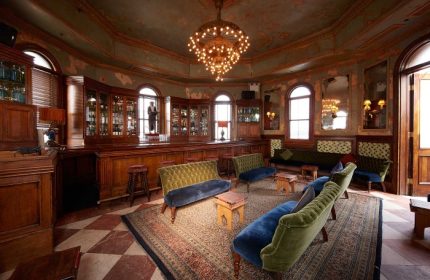 The Jane Hotel, a most-booked gay hotel near gay bars in New York City. Ornate bar area with velvet couches, chandelier, and vintage decor.