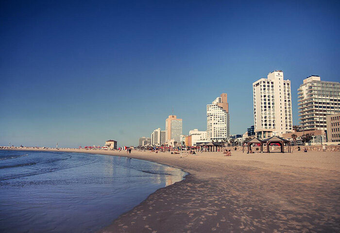 Tel Aviv beach view near Brown TLV Hotel, a most-booked gay hotel. Sandy shore, blue sky, and city skyline. Perfect for gay travel advice.