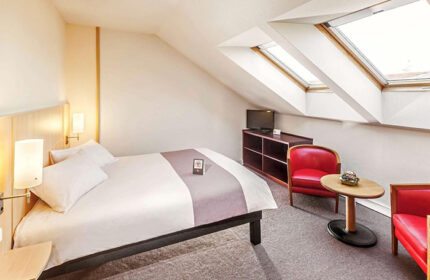 Ibis Praha Wenceslas Square Hotel room. Gay-friendly Prague hotel with skylights, bed, TV, and red chairs. Great location near gayborhood.