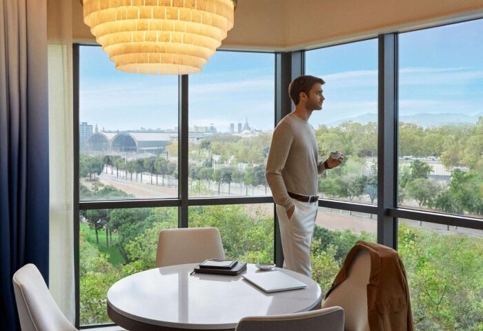 Sofitel Barcelona Skipper hotel room view. Man looks out at Barcelona city. Most booked gay hotels in Barcelona beach.