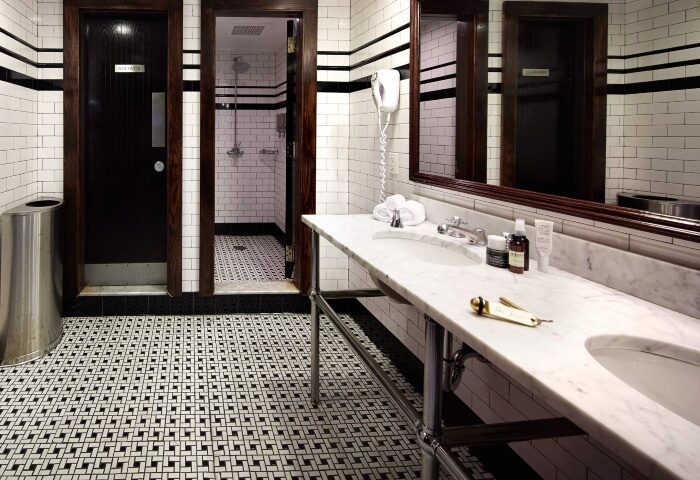 The Jane Hotel bathroom. One of the most booked gay-friendly hotels in New York. Black and white tiled floor, marble counter and dark wood doors.