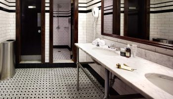 The Jane Hotel bathroom. One of the most booked gay-friendly hotels in New York. Black and white tiled floor, marble counter and dark wood doors.