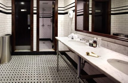 The Jane Hotel bathroom. One of the most booked gay-friendly hotels in New York. Black and white tiled floor, marble counter and dark wood doors.